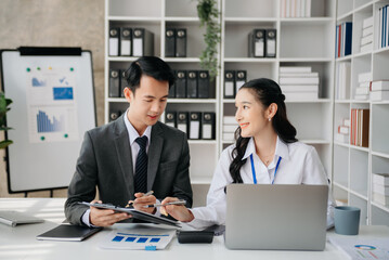 Fototapeta premium Asian business colleague business presents and explains and using laptop and tablet. Teamwork, financial marketing team, while sitting in office room.