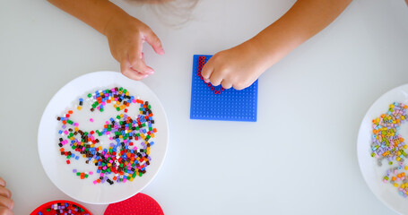Little girl makes figure from bead on the table at home, top view