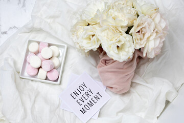 Fototapeta na wymiar Feminine Inspirational Flatlay Enjoy Every Moment with marshmallows and white Roses