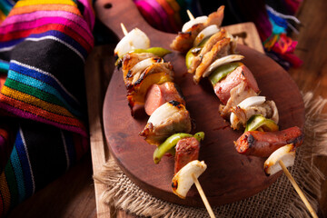 Homemade Skewers with meat and grilled vegetables served on a rustic wooden board, also known as...