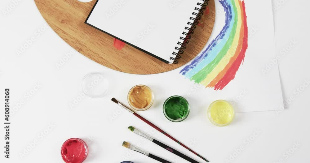Poster overhead view of notebook, brushes and paints on white background with copy space, in slow motion