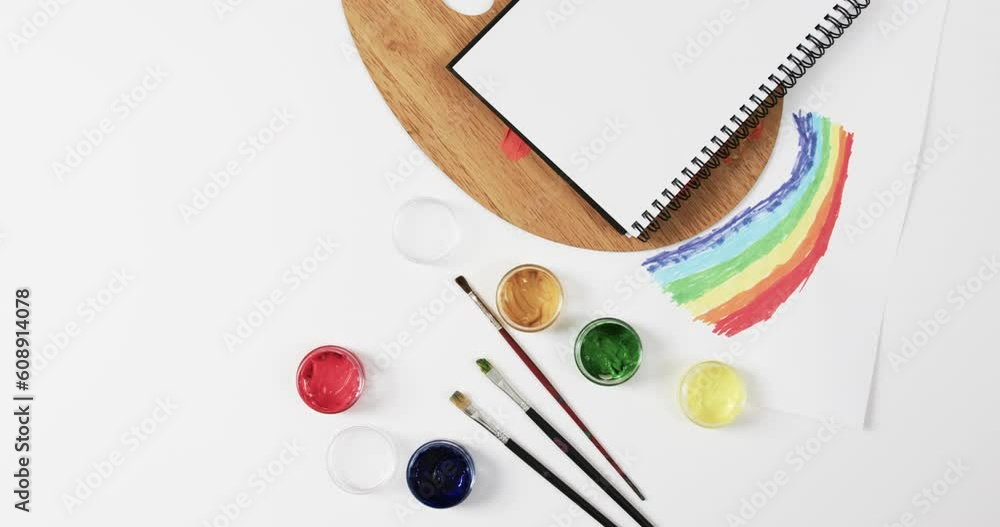 Poster overhead view of notebook, brushes and paints on white background with copy space, in slow motion