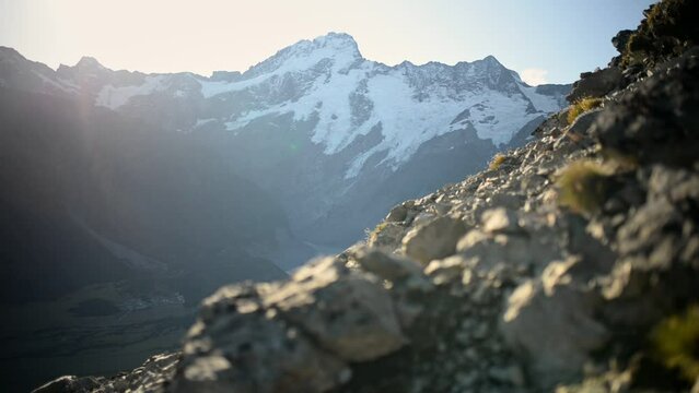 Steep rocky slope bathed in golden sunlight, snowy Mount Sefton in background
