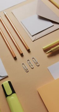 Vertical video of close up of pencils and stationery arranged on beige background, in slow motion