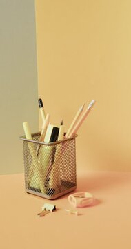 Vertical video of close up of school stationery in cup on yellow background, in slow motion
