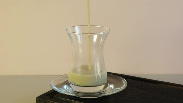 Traditional thick oriental tea with milk and spices is poured into armudu cup. Karak tea or Masala chai in glass. Indian spicy drink. Video, 4K. Slow motion.