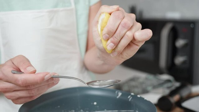 In slow motion, the pastry chef squeezes half a lemon into a spoon and pours the juice into the white cake batter.