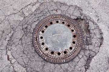 Cast iron old manhole cover in cracked asphalt, top view