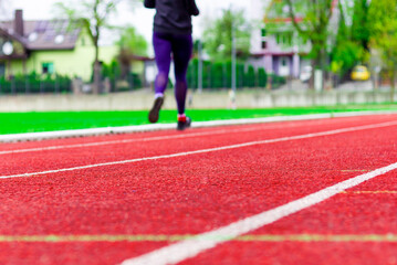 Fototapeta premium A woman in sportswear sprinting on running track at stadium on summer day.Healty lifestyle.Back view.Selective focus on the ground,copy space.