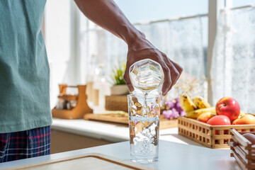 Close-up hands Asian man in casual clothes on holiday morning, was holding jug water in hand and pouring water in jug into drinking glass, after good night's sleep, drink glass water for good health.