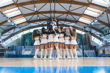 Cheerleaders female team practicing, holding a girl in the air on the basketball court. High...