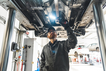 Auto mechanic with LED work light inspecting car chassis standing under it . High quality photo