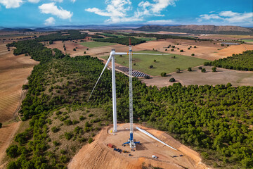Aerial view of a wind turbine blade is moving up by a giant crane to be mounted on the nacelle of a wind farm under construction. Team of professional with a giant crane lifting a blade. Spain - obrazy, fototapety, plakaty