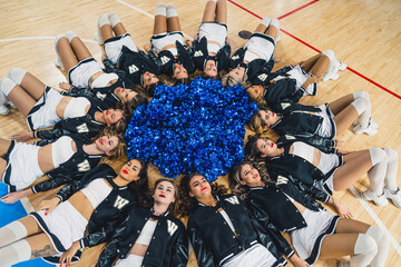 Overhead view of cheerleaders girls lying on the floor forming a circle with pom poms in the...