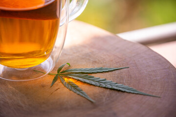 A hot cannabis tea beverage in a glass cup sitting on a wooden table alongside a glass mug.