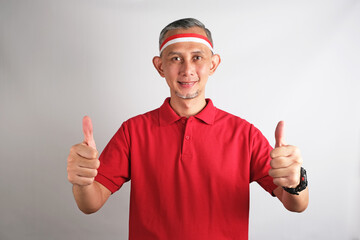 Portrait of Asian Man wearing red and white Indonesia flag attribute looks happy doing positive...