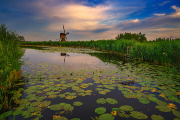Sunset over an old dutch windmill by a river in Kinderdijk, Netherlands. This system of 19...