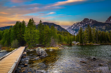 Sunset over Taggart Lake and Grand Teton Mountains in Wyoming, USA, with a footbridge in the...