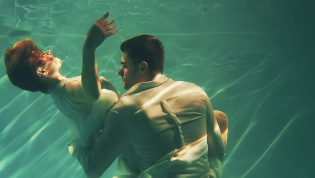 Happy fantasy couple fall in love swim dive man king and woman fashion model posing underwater dark blue sea. Wet white dress. fairy sexy girl Muse river nymph swims hugs guy magic under water pool 4k