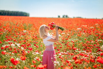 blonde woman in a poppy field with daisies. A girl with a bouquet of red and white flowers