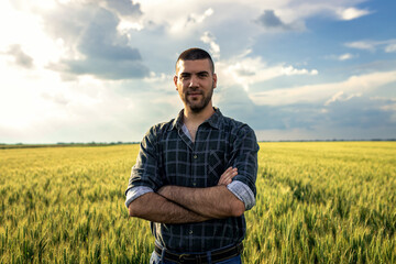 Portrait of young farmer standing in a green wheat field examining crop.