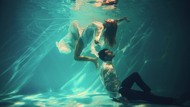 Happy fantasy couple fall in love swim dive man king and woman fashion model posing underwater dark blue sea. Wet white dress. fairy sexy girl Muse swims guy magic under water pool 4k. Themed wedding 