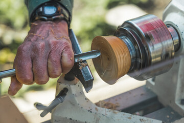 Closeup shot of male carpenter artist creating wooden art pieces with the use of lathe. Outdoor shot. Dutch town. High quality photo