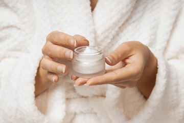 Young woman in bathrobe holds jar of cosmetic
