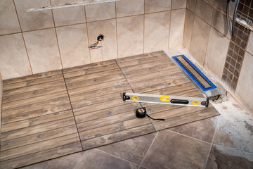 Linear floor level shower. Wood effect ceramic tile and modern metallic linear drain installation...