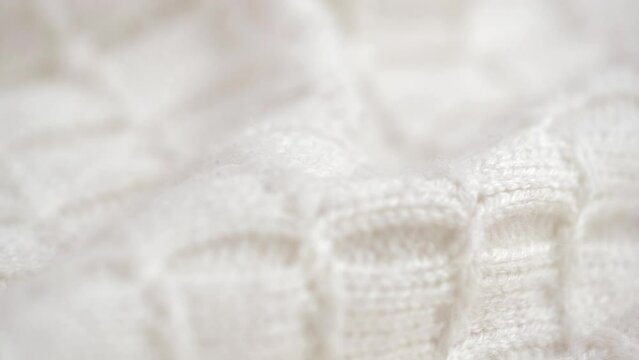 texture of crumpled knitted woolen clothes with pattern of natural wool closeup. rotation. soft knitted wool fabric in white. cozy woolen fabric, knitwear, warm sweater. macro.