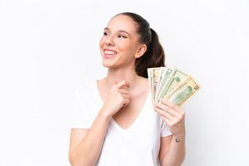 Young caucasian woman taking a lot of money isolated on white background looking to the side and smiling