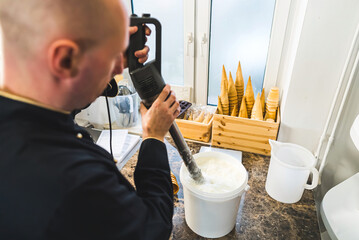 Hands of a chef preparing ice cream for waffle cones using a blender in a bucket. High quality photo