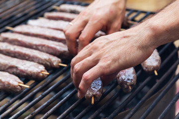 The hands of the cook take raw, minced meat on wooden sticks from a metal bowl.