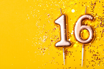 Gold candles in the form of number sixteen on yellow background with confetti. 16 years celebration.