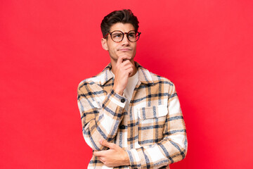 Fototapeta premium Young caucasian handsome man isolated on red background having doubts and thinking