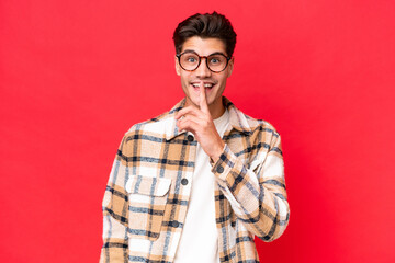 Young caucasian handsome man isolated on red background showing a sign of silence gesture putting finger in mouth