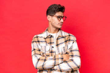 Fototapeta premium Young caucasian handsome man isolated on red background keeping the arms crossed