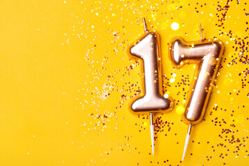 Gold candles in the form of number seventeen on yellow background with confetti. 17 years celebration. - obrazy, fototapety, plakaty