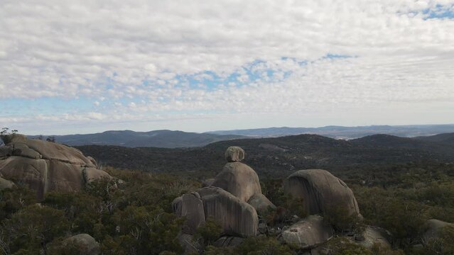 Ancient granite pinnacle bearing a massive balancing topside tor towering over the scenic landscape. Panning drone view