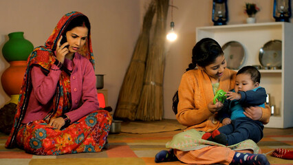 A young girl from an Indian village playing with her little sister - Village home . A rural housewife in a saree and a sweater talking on the mobile while sitting in her traditional kitchen - leisu...