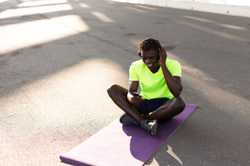 Young athlete man listening music while resting after training. Handsome African man training outside.