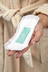 Clean new feminine sanitary pad in an elegant female hand with a beautiful manicure against the background of a body in a beige bathrobe. - 608976669