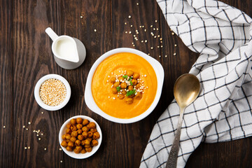 Autumn Vegetarian pumpkin and carrot cream soup with chickpeas and herbs on dark wooden background. Comfort food, fall and winter healthy slow food concept.