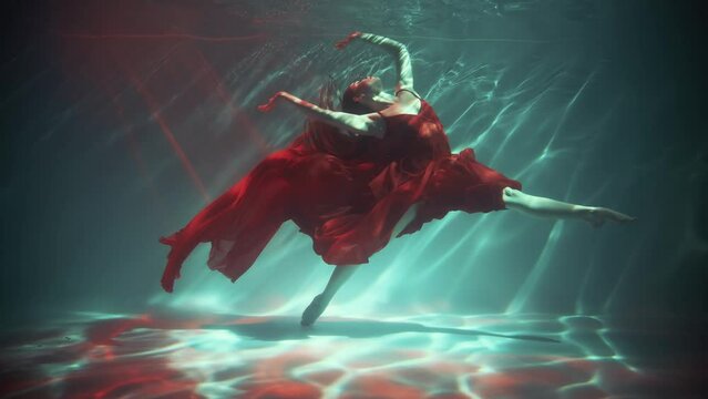 Sexy girl fashion model posing underwater for creative photo video shooting, waving long legs in twine. Fantasy queen woman swims soars in dark water neon blue red light. Art silk long dress. pool 4k