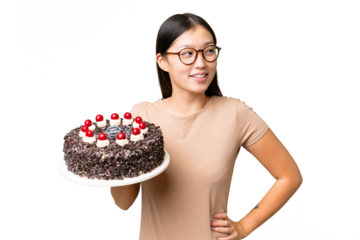 Young Asian woman holding birthday cake over isolated chroma key background posing with arms at hip and smiling