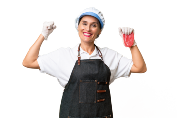 Butcher woman wearing an apron and serving fresh cut meat over isolated background doing strong gesture