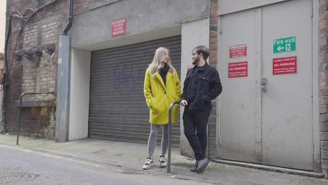 A young woman and man standing in an alleyway chatting, locked off