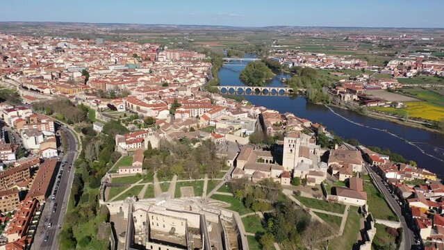 Picturesque aerial view of Zamora city overlooking brownish tiled roofs of residential buildings and ancient arched bridge over Duero river on spring day, Spain