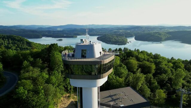 Panoramic view from the drone during sunset, on the Solińskie lake overlooking the modern gondola cable car with the lookout tower over the Solina water dam, in the Polish Bieszczady Mountains, Poland