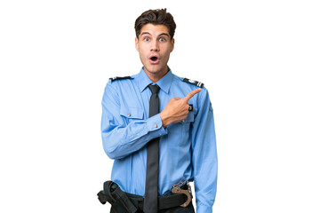Young police man over isolated background surprised and pointing side